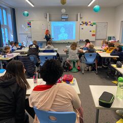 Eine Schulklasse sitzt vor der Leinwand und schaut die Präsentation an.